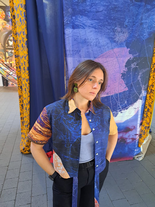 Woman wearing a colorful cropped shirt standing in front of a textured blue and yellow fabric backdrop which has the same print as the shirt