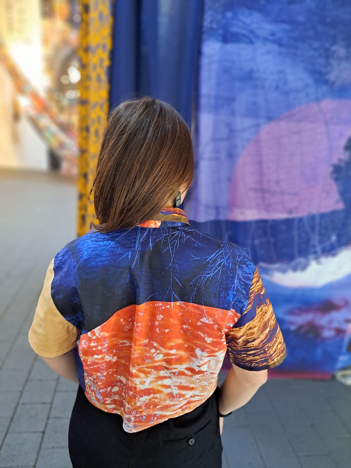 Person wearing a colorful shirt with a blue and orange pattern, standing in front of a fabric print with the same pattern.