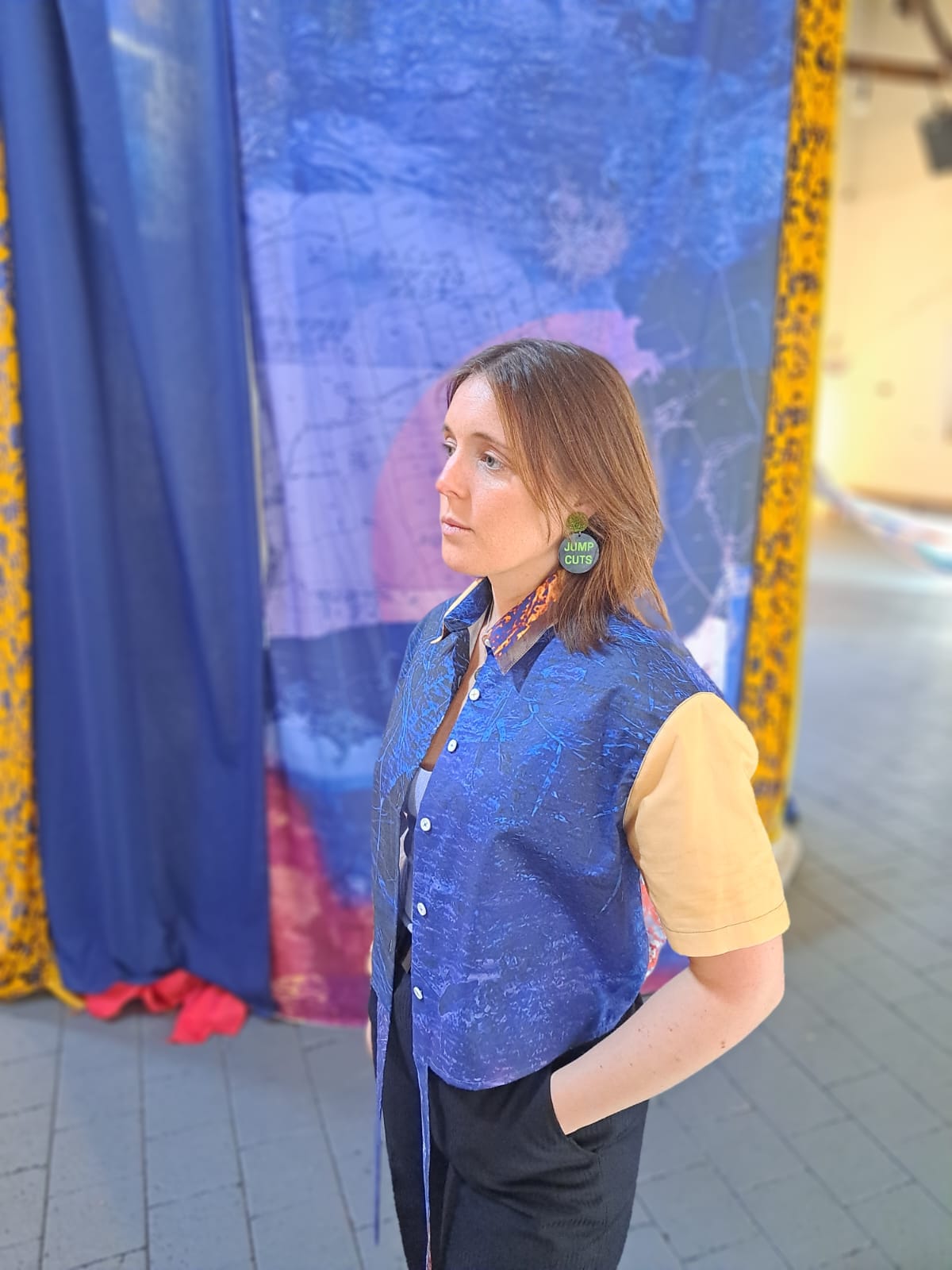Person wearing a colorful shirt with a blue and orange pattern, standing in front of a fabric print with the same pattern.